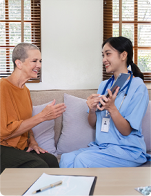 Healthcare professional discussing with a patient at home, holding a tablet and smiling, promoting in-home medical care.