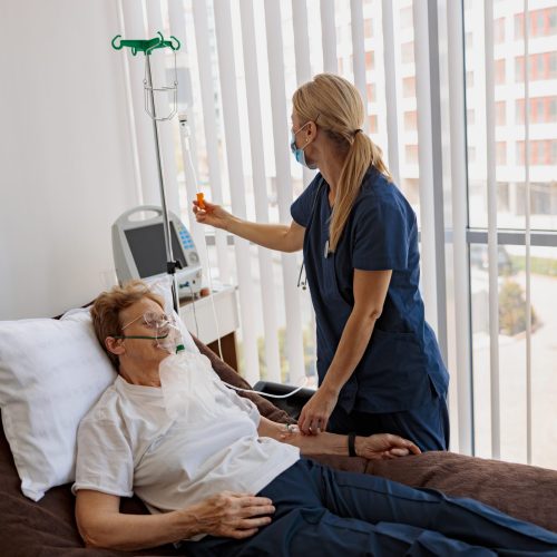 Nurse putting a drip on the arm of her patient in mask during pandemic of Covid 19